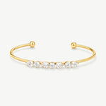 A gold open cuff bracelet featuring a row of clear marquise and round-cut gemstones across the front, displayed on a clean off-white background.