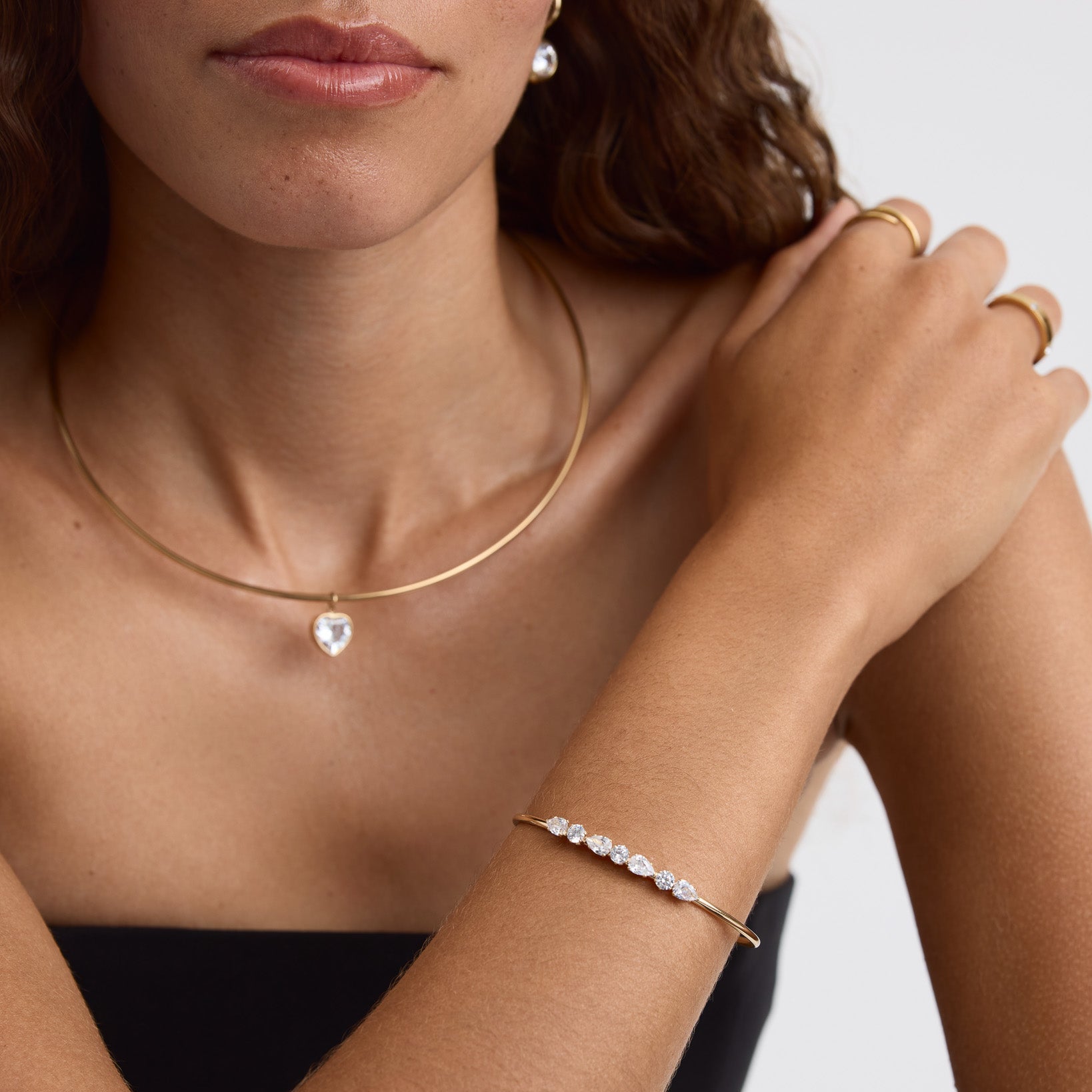 A close-up lifestyle shot of a model wearing a delicate gold caged necklace with a clear teardrop crystal pendant and a matching gold crystal-studded bracelet.