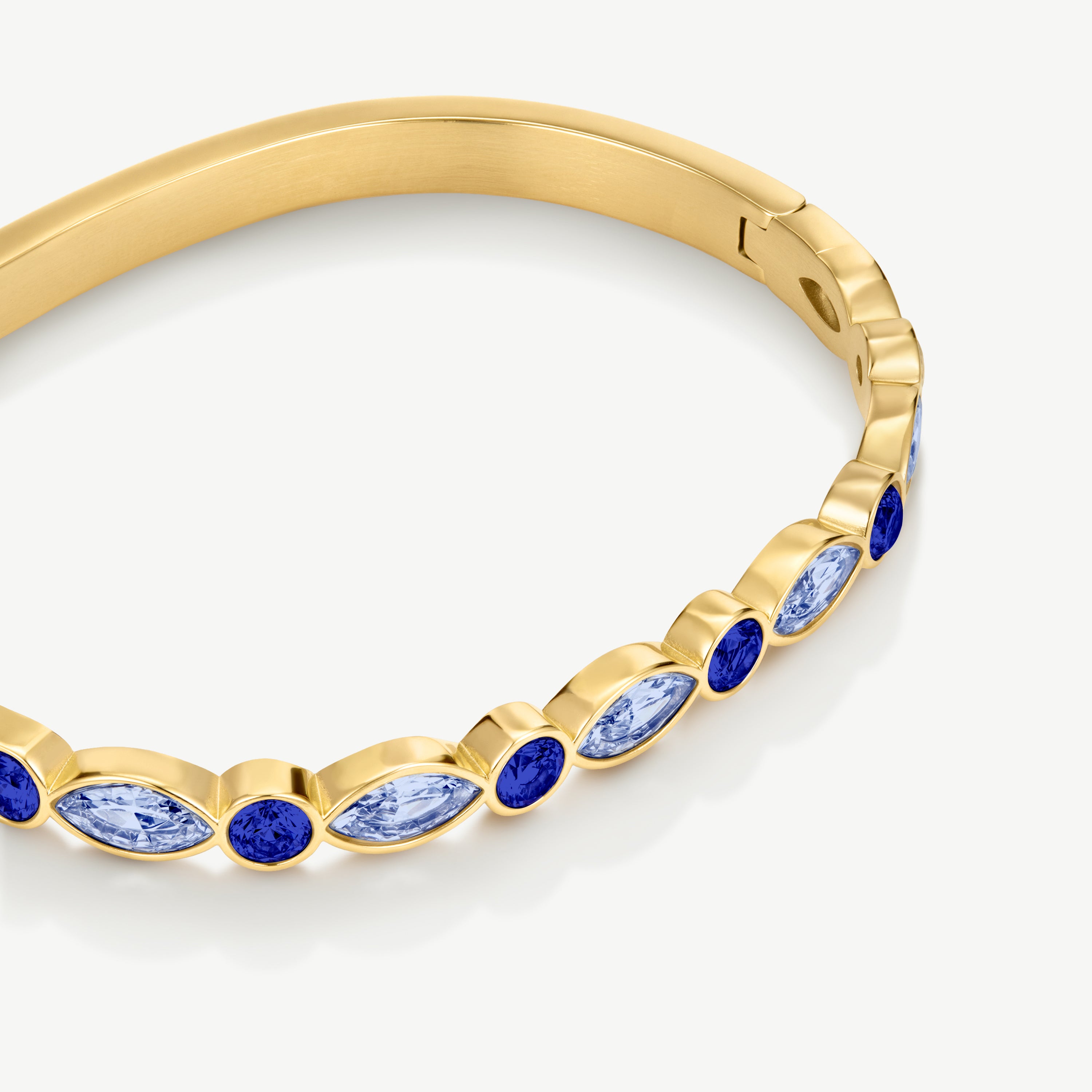 A close-up of a gold bangle bracelet featuring alternating round and marquise-cut blue gemstones in gold bezel settings, shown on a clean white background.
