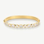 A gold bangle bracelet featuring a row of bezel-set marquise and round clear gemstones, shown on a light gray background.
