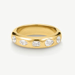 A polished yellow gold band ring featuring five clear gemstones in marquise, rectangular, and round shapes, set against a clean off-white background.