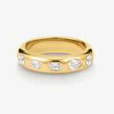 A polished yellow gold band ring featuring five clear gemstones in marquise, rectangular, and round shapes, set against a clean off-white background.