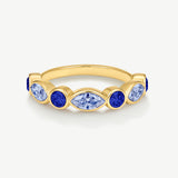 A gold band ring featuring a row of marquise-cut and oval-cut blue gemstones, photographed on a clean, light off-white background.