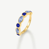 A gold ring featuring a vertical row of marquise-cut light blue and round-cut dark blue gemstones, set against a clean off-white background.