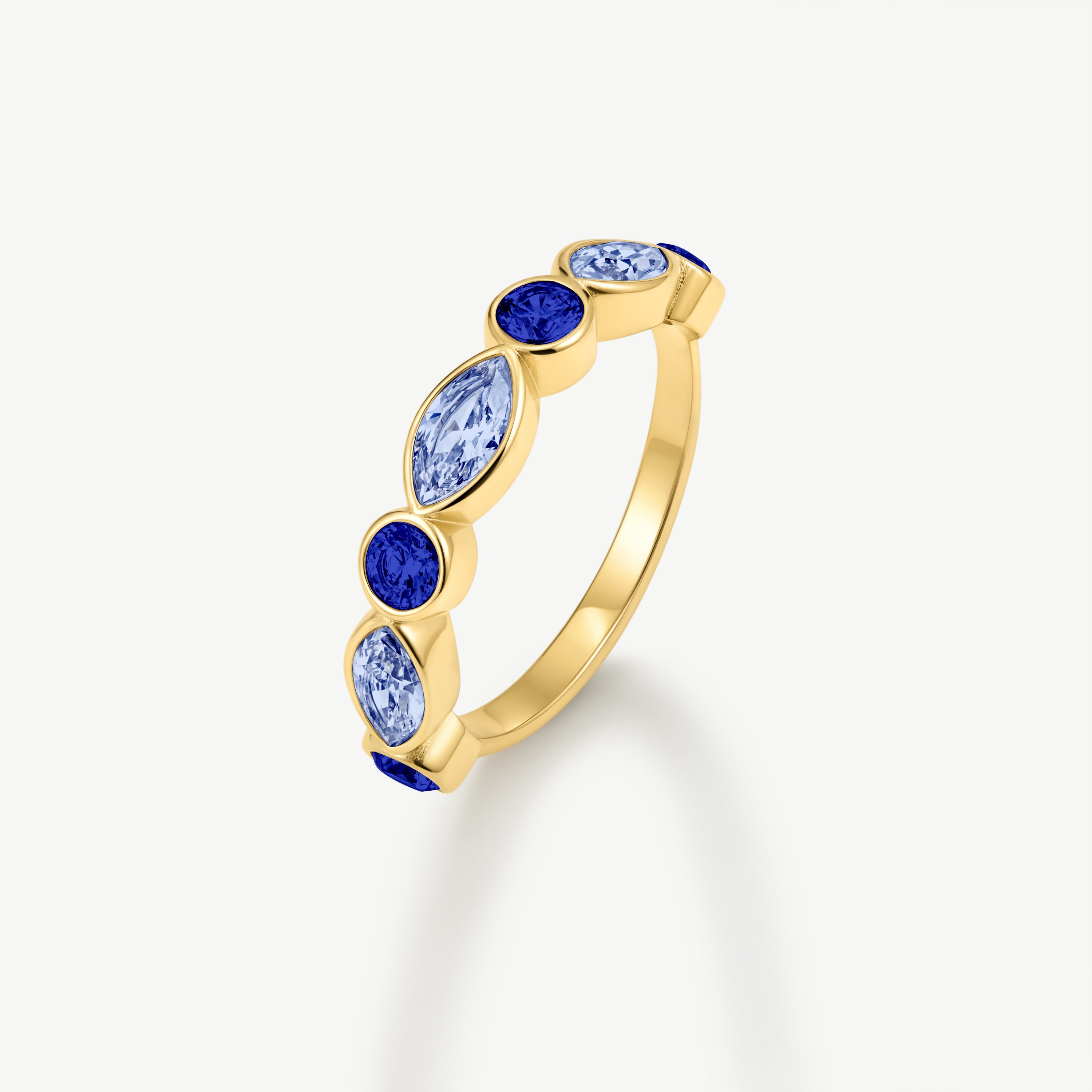 A gold ring featuring a vertical row of marquise-cut light blue and round-cut dark blue gemstones, set against a clean off-white background.
