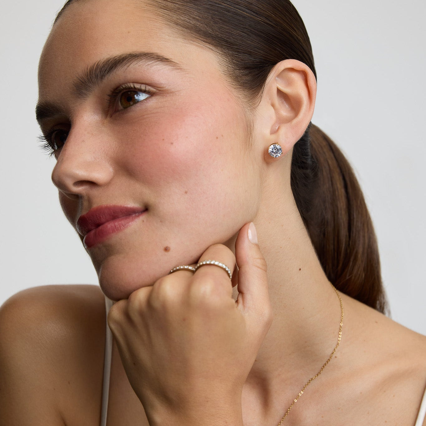 Woman wearing earrings and a necklace, touching her neck with one hand.