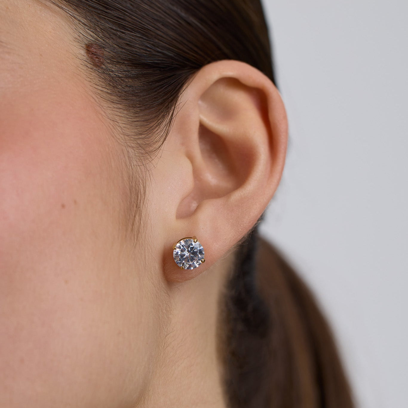 Close-up of a person wearing a diamond stud earring against a neutral background